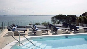 Zona de piscina con sillones de descanso y vista al mar.
