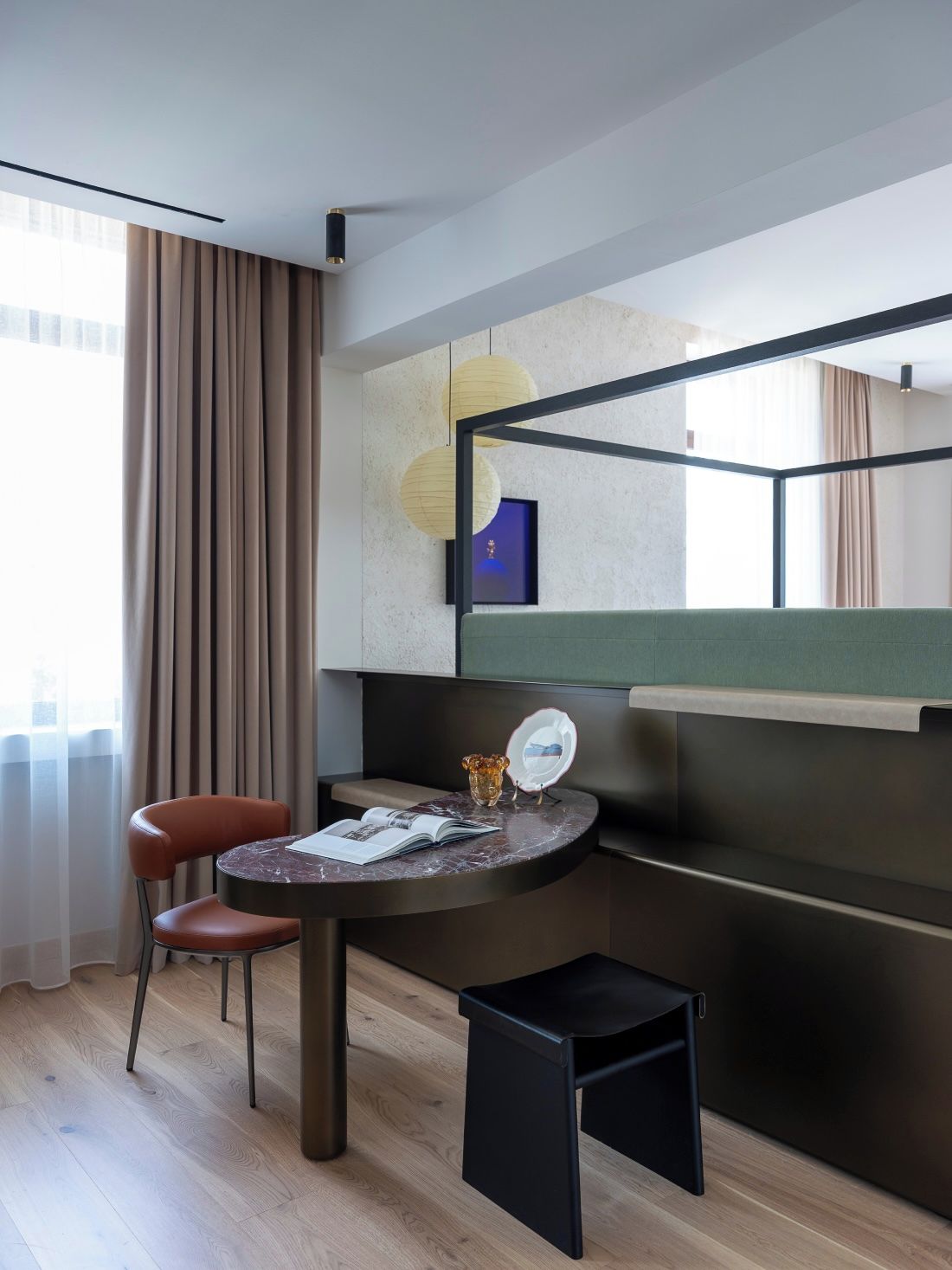 Habitación de hotel moderna con una cama curvada, una mesita redonda con un libro, una silla y una mesita de noche con un jarrón.