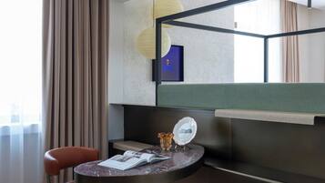 Habitación de hotel moderna con una cama curvada, una mesita redonda con un libro, una silla y una mesita de noche con un jarrón.