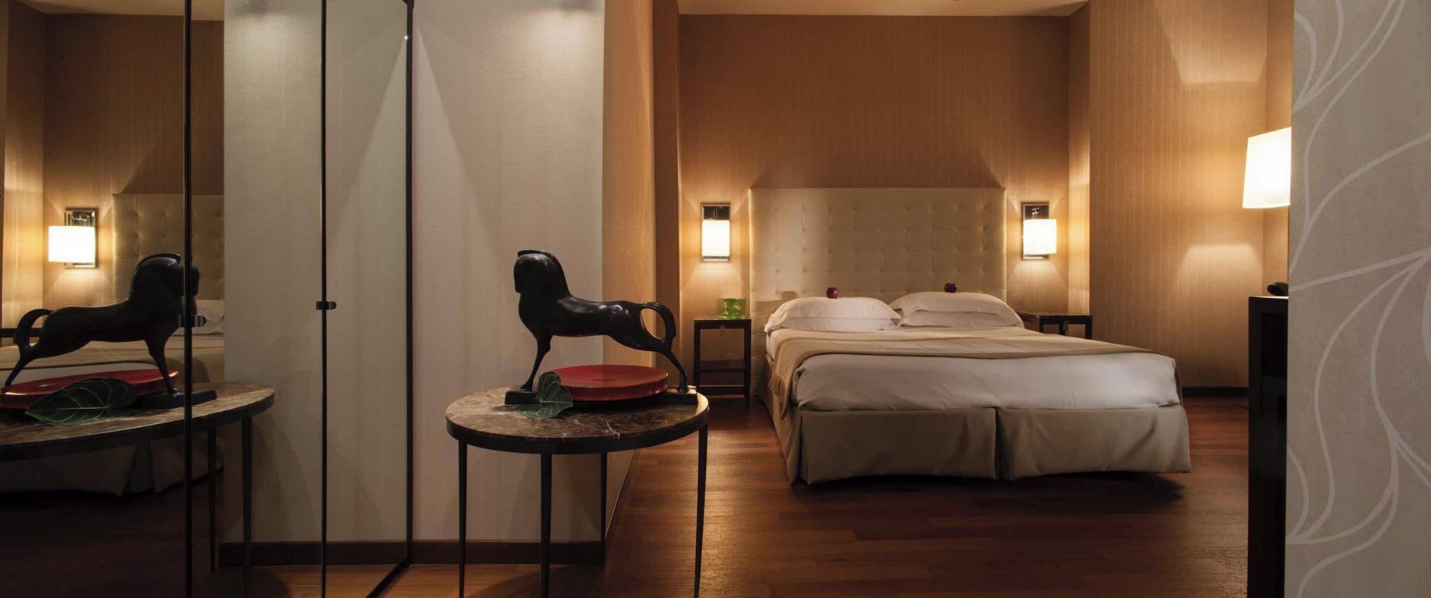 Habitación de hotel con cama, una mesita pequeña con silla y dos lámparas fijadas a la pared.