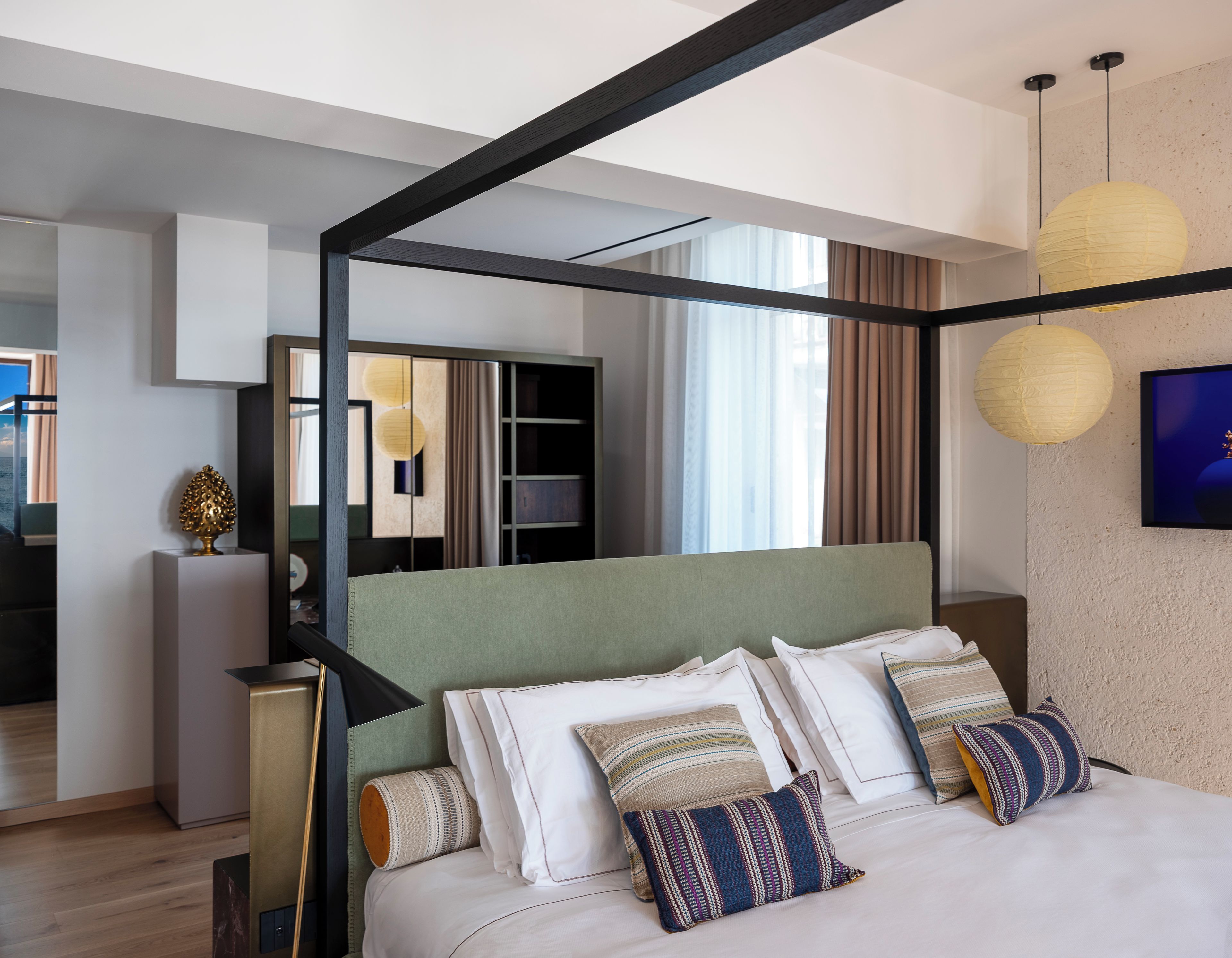 A modern bedroom with a four-poster bed, a large mirror, and a view of the sea.