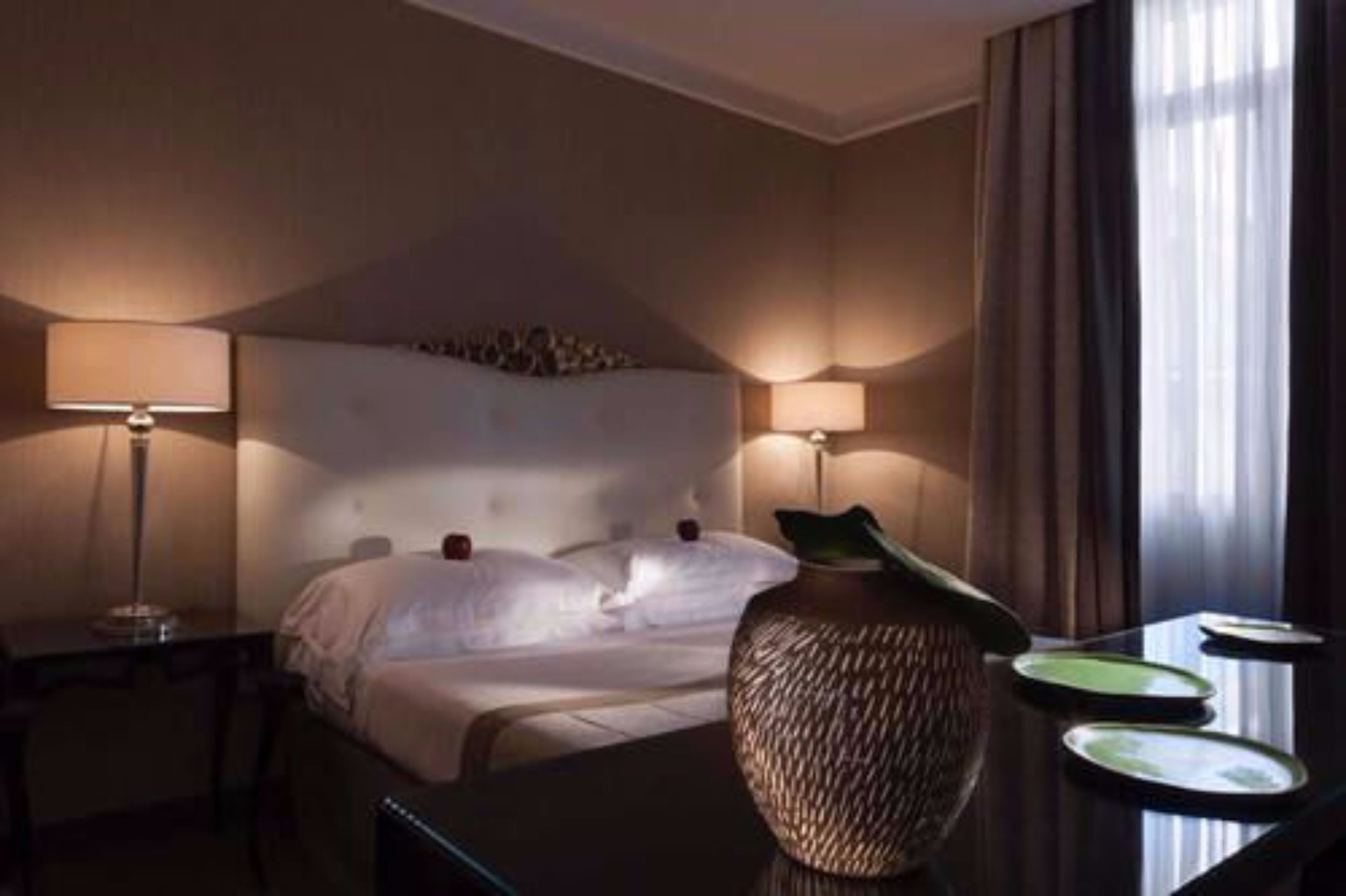 Een hotelkamer met een groot bed, twee bedlampen, een vaas en een tafel met borden.
