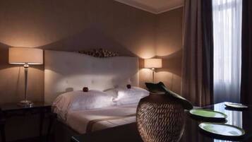 Een hotelkamer met een groot bed, twee bedlampen, een vaas en een tafel met borden.