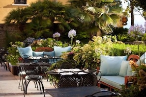 An outdoor seating area with tables and chairs, surrounded by lush greenery and plants.
