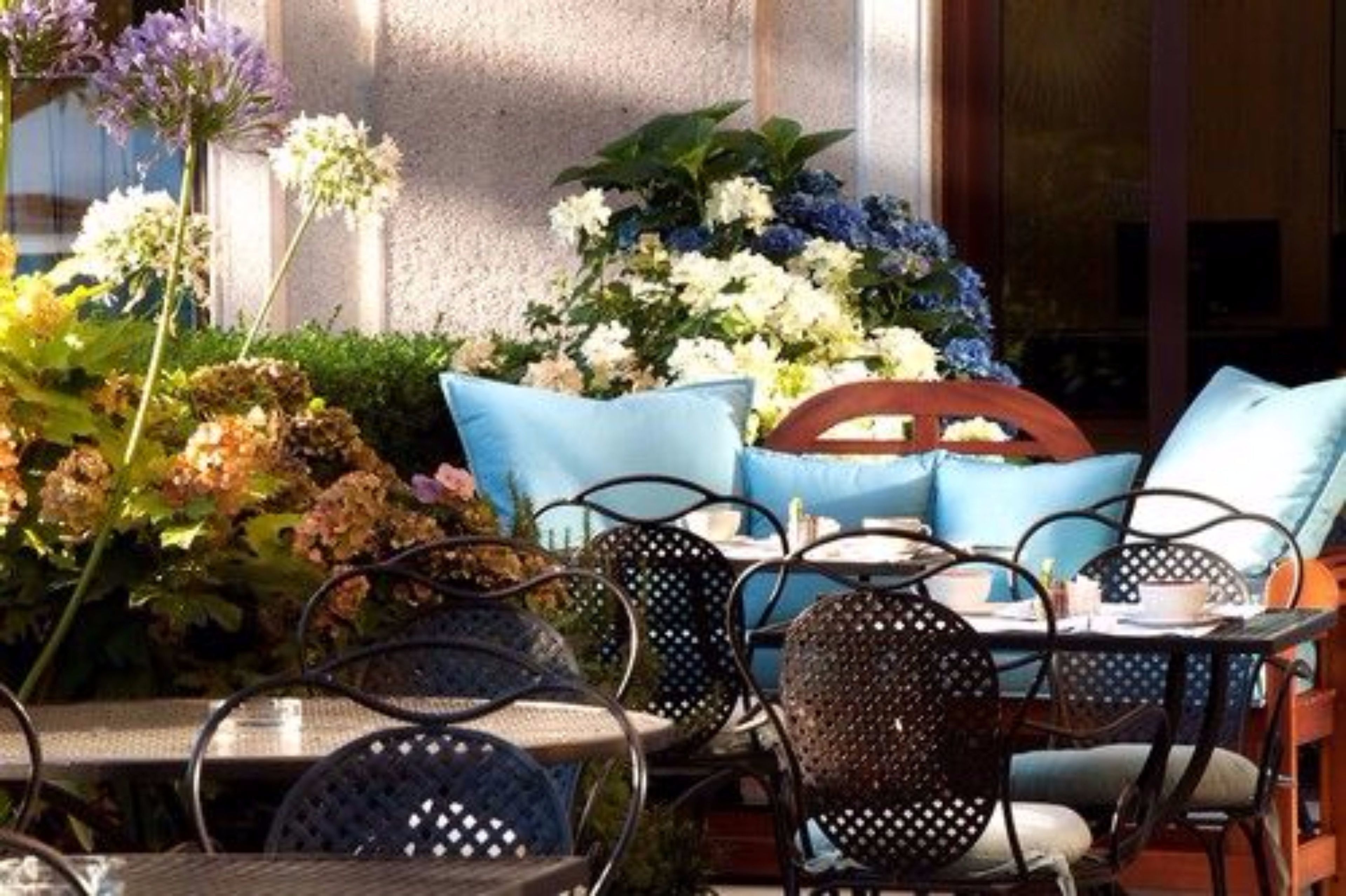 An outdoor seating area with metal chairs and tables, surrounded by various flowers and plants.