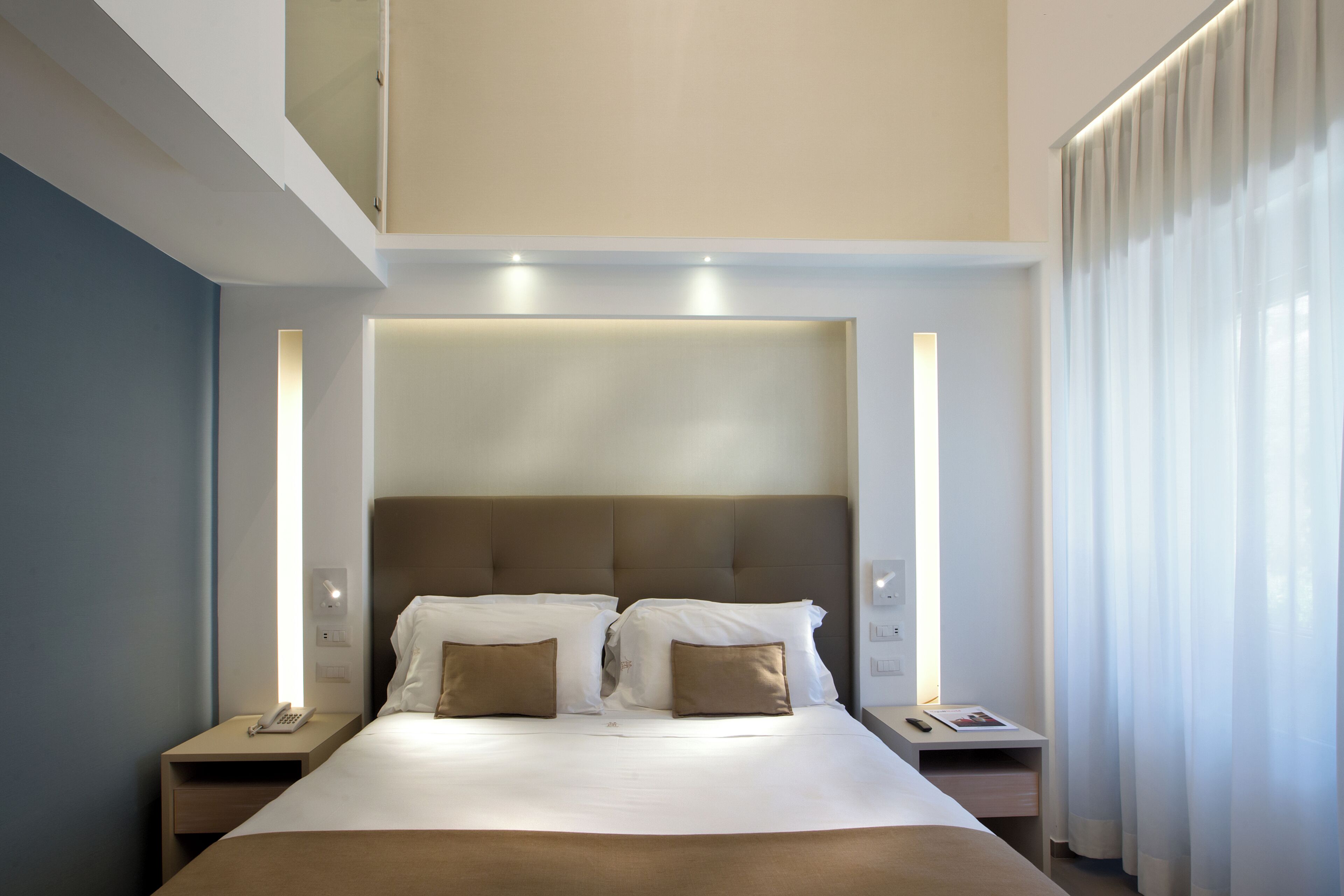 A modern hotel room with a large bed, two bedside tables with lamps, and a large window with curtains.