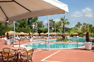 Un'area piscina con lettini e ombrelloni, circondata da palme e un cielo sereno.