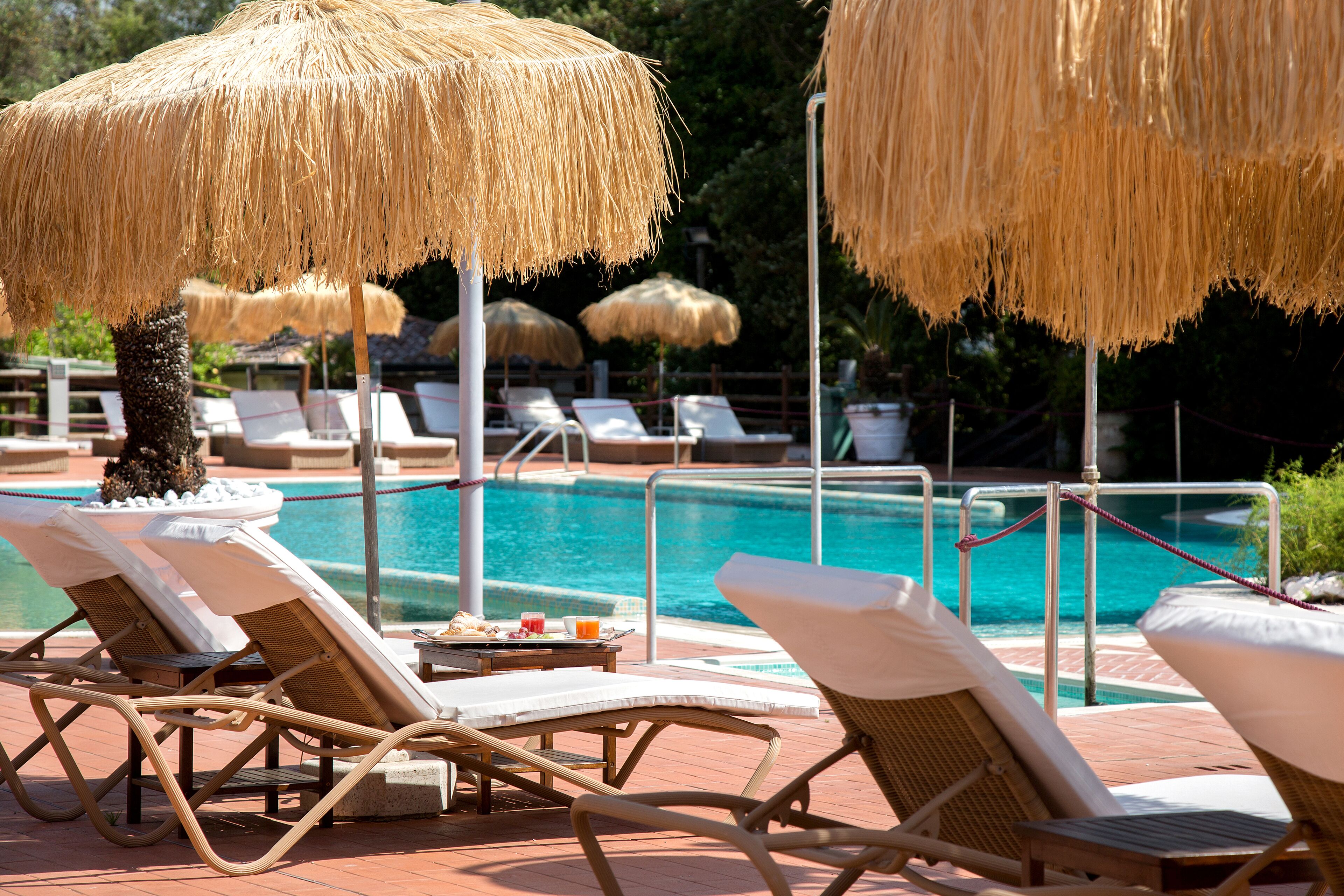 A poolside area with lounge chairs and thatched umbrellas, a pool, and a brick walkway.