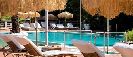 A poolside area with lounge chairs and thatched umbrellas, a pool, and a brick walkway.