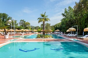 Una piscina con lettini e ombrelloni, circondata da palme e vegetazione.