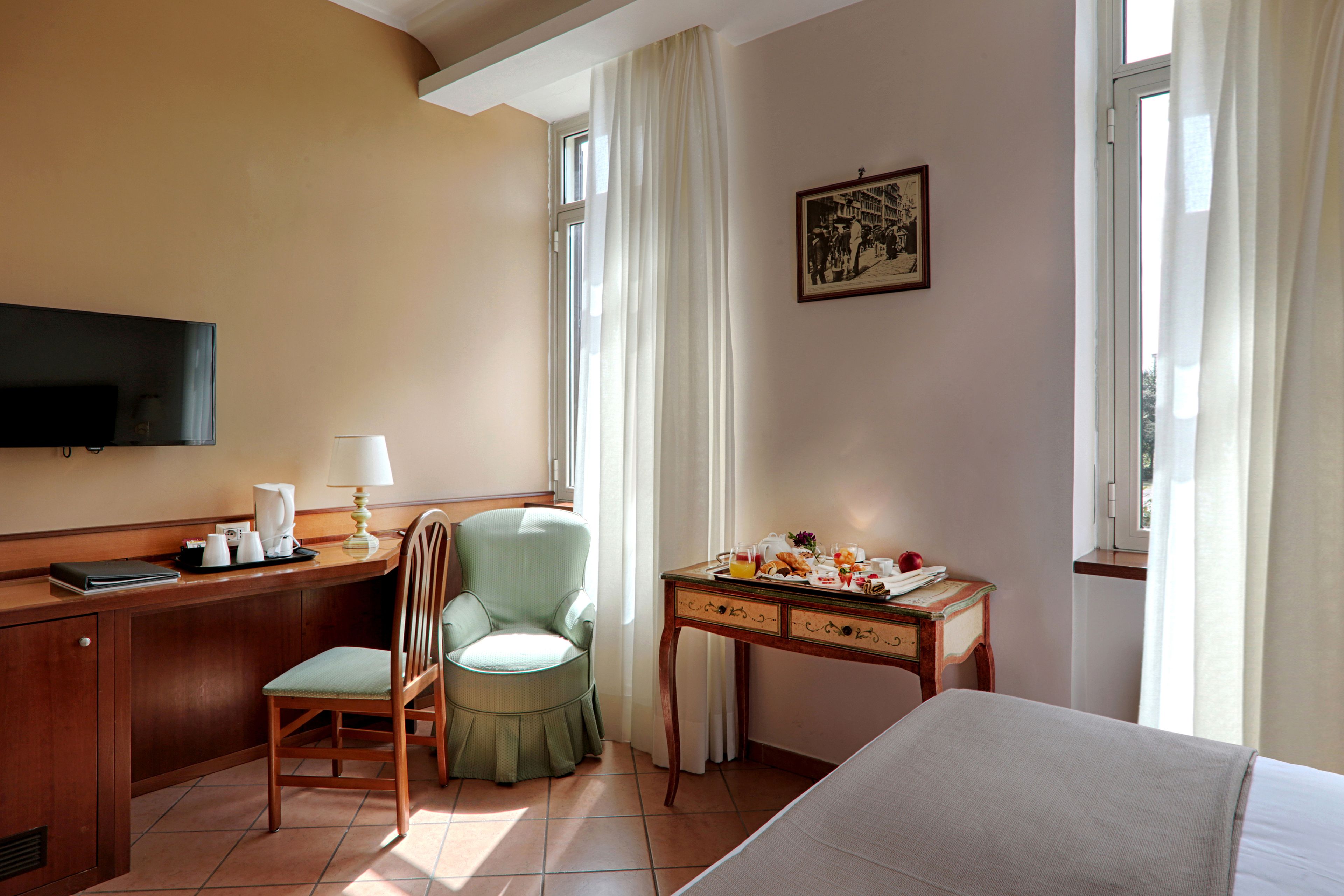 Habitación de hotel con cama, escritorio con lámpara, silla, televisor y mesa de comedor con productos para el desayuno.