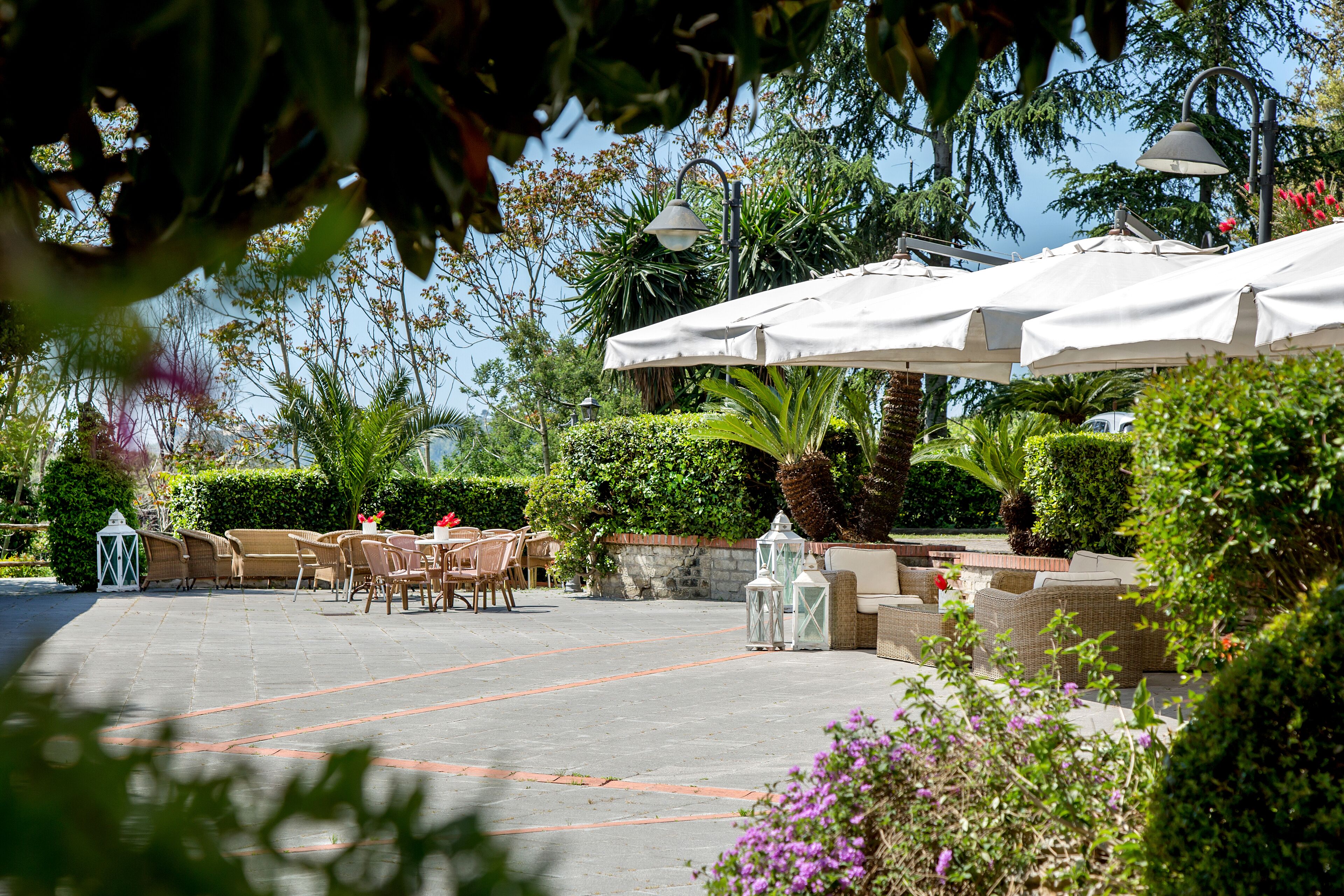 Un espace extérieur aménagé en terrasse, avec des tables et des chaises, entouré de verdure et agrémenté de parasols.