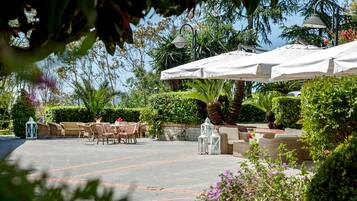 Un espace extérieur aménagé en terrasse, avec des tables et des chaises, entouré de verdure et agrémenté de parasols.