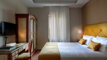 A hotel room with a bed, a desk with a flat-screen TV, a telephone, and a lamp.