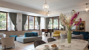 A modern hotel room with a marble dining table, a piano, and a sofa with blue cushions. - Montespina Park Hotel (Naples)