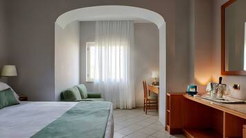 Ein Hotelzimmer mit einem Bett, einem Schreibtisch und einem Stuhl. Es gibt ein Fenster mit Vorhängen, eine Lampe und einen Spiegel an der Wand.