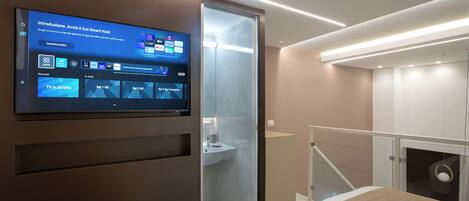 A modern hotel room with a large flat-screen TV mounted on the wall displaying a hotel app interface.