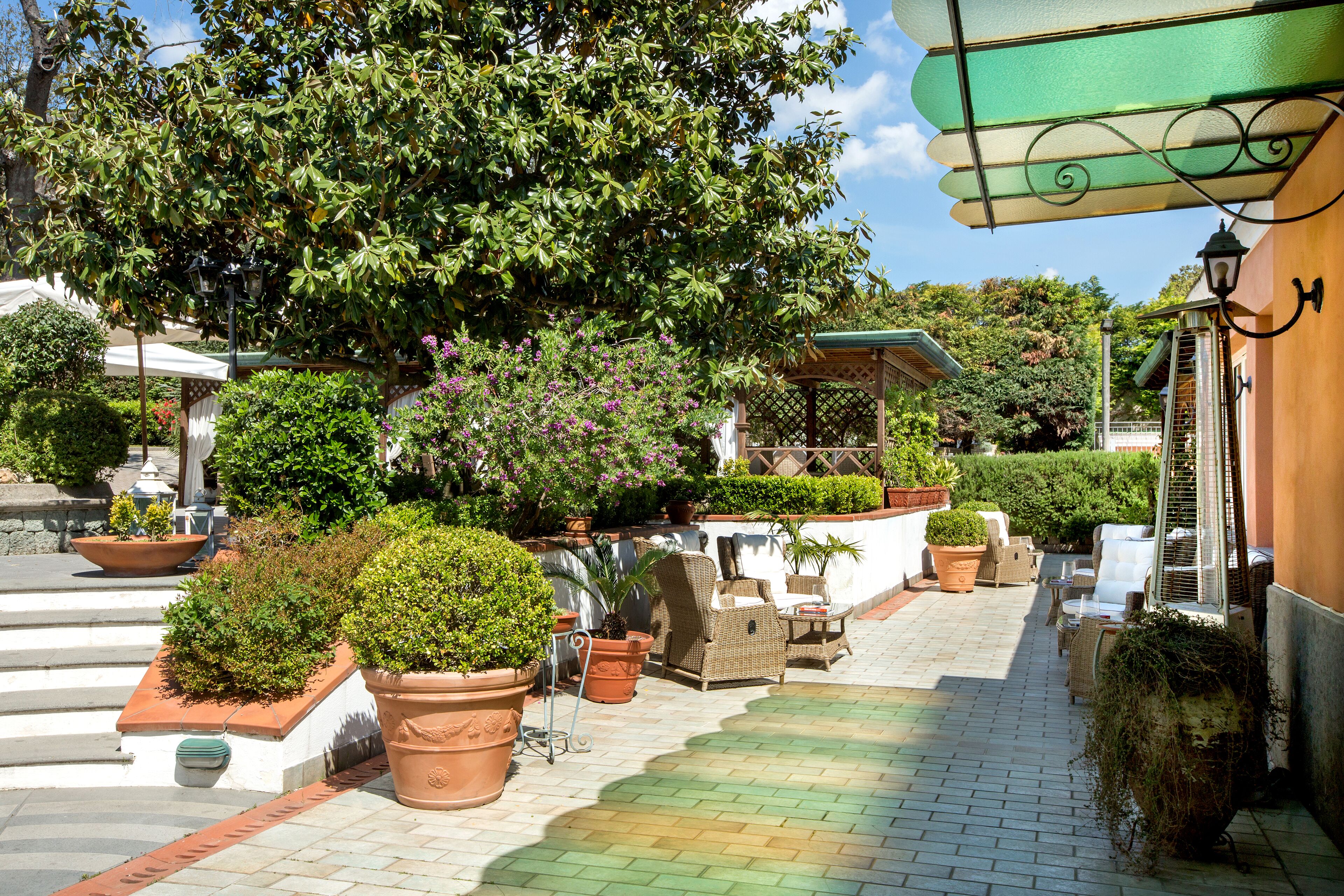 Een terras met plantenpotten, rieten meubels en een pergola.