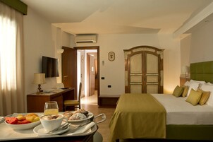 Una camera d'albergo con un letto, un tavolo per la colazione, una televisione e un armadio.