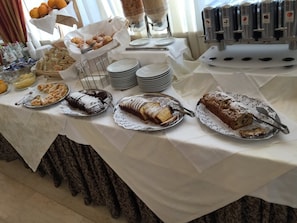 Een buffet met diverse gebakjes, taarten en een fruitmand.