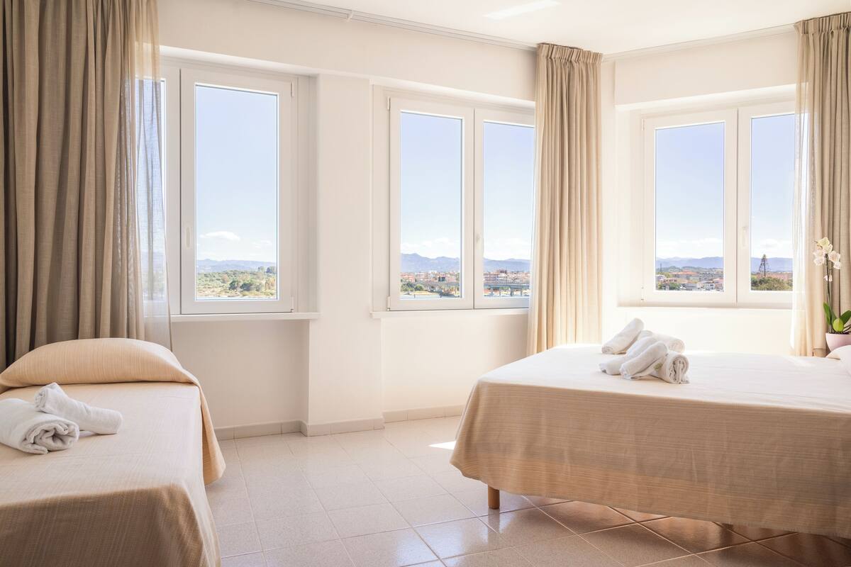Une chambre d’hôtel avec deux lits, de grandes fenêtres offrant une vue sur la ville et les montagnes, ainsi qu’une vue sur le ciel.