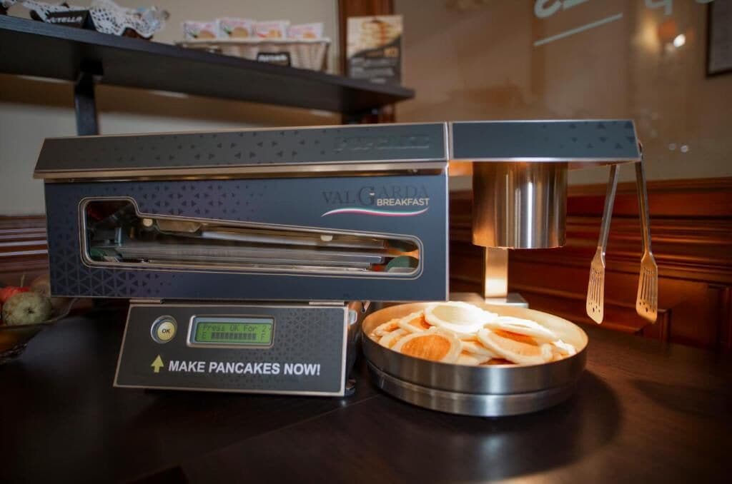 A commercial kitchen with a branded appliance for making pancakes, a digital display, and a stainless steel bowl with pancake ingredients.