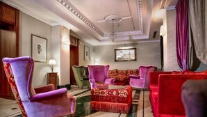A spacious lobby with a red and purple sofa set, a green armchair, and a chandelier. - LH Hotel Andreotti (Rome)