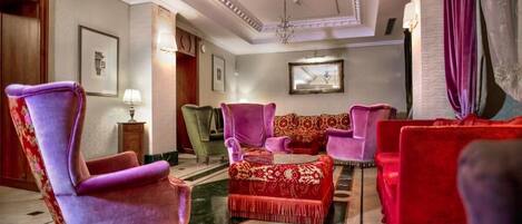 A spacious lobby with a red and purple sofa set, a green armchair, and a chandelier.