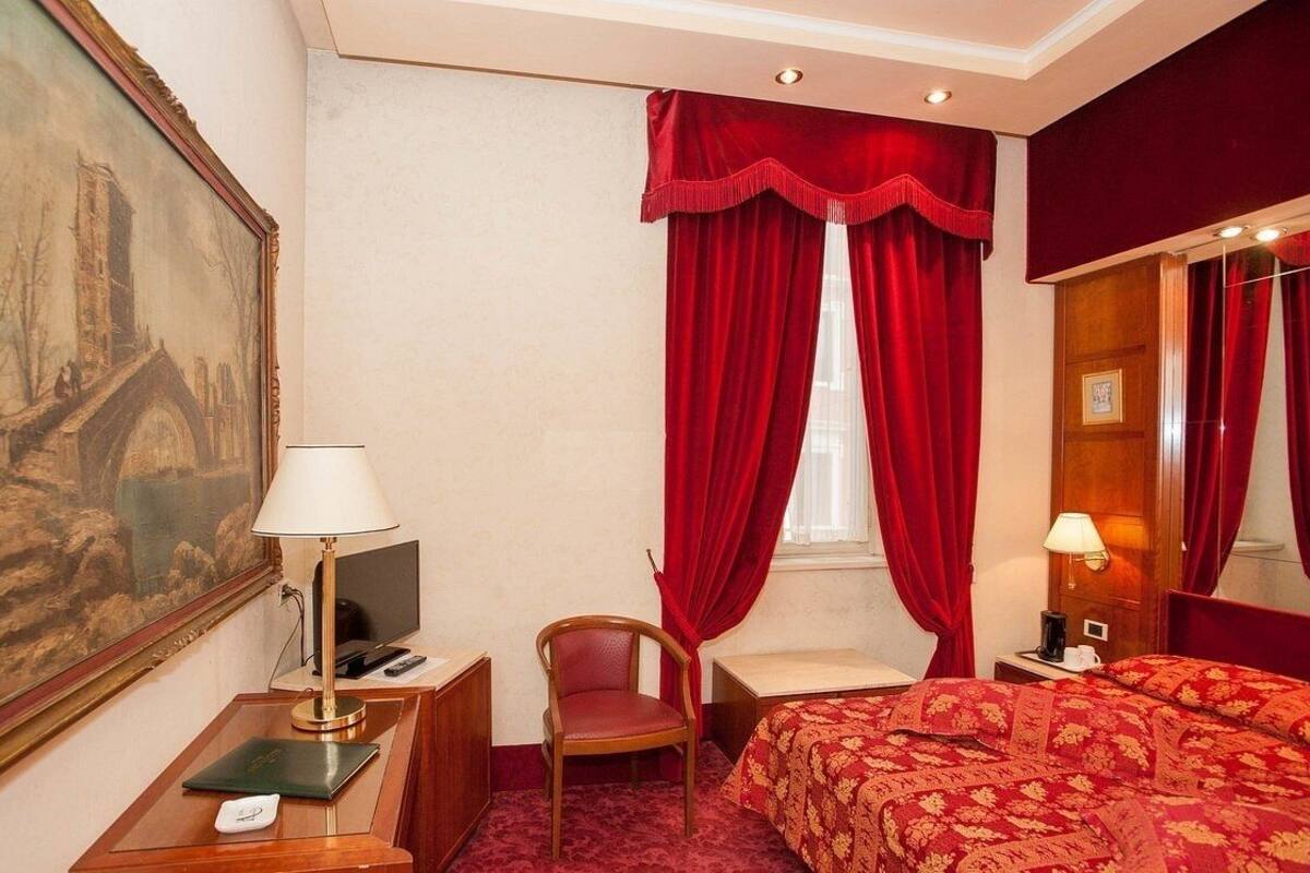 Une chambre d’hôtel avec un lit, une chaise, un bureau avec une lampe, une télévision et un tableau au mur.