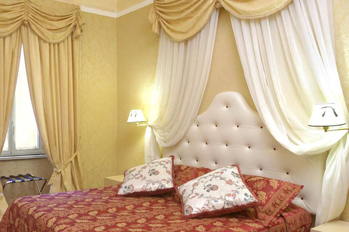 Une chambre à coucher avec une tête de lit capitonnée, un lit avec une literie à motifs floraux, deux oreillers et des rideaux.