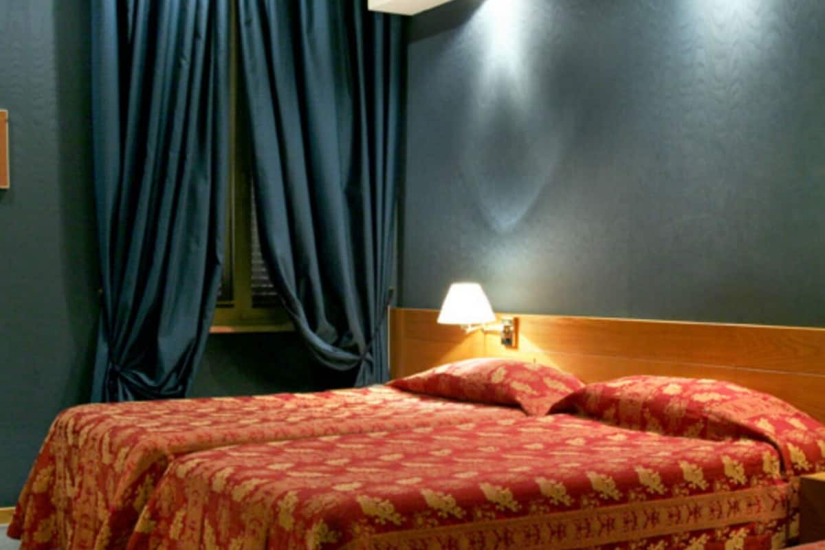 Une chambre d’hôtel avec deux lits, des murs sombres et une fenêtre avec des rideaux.