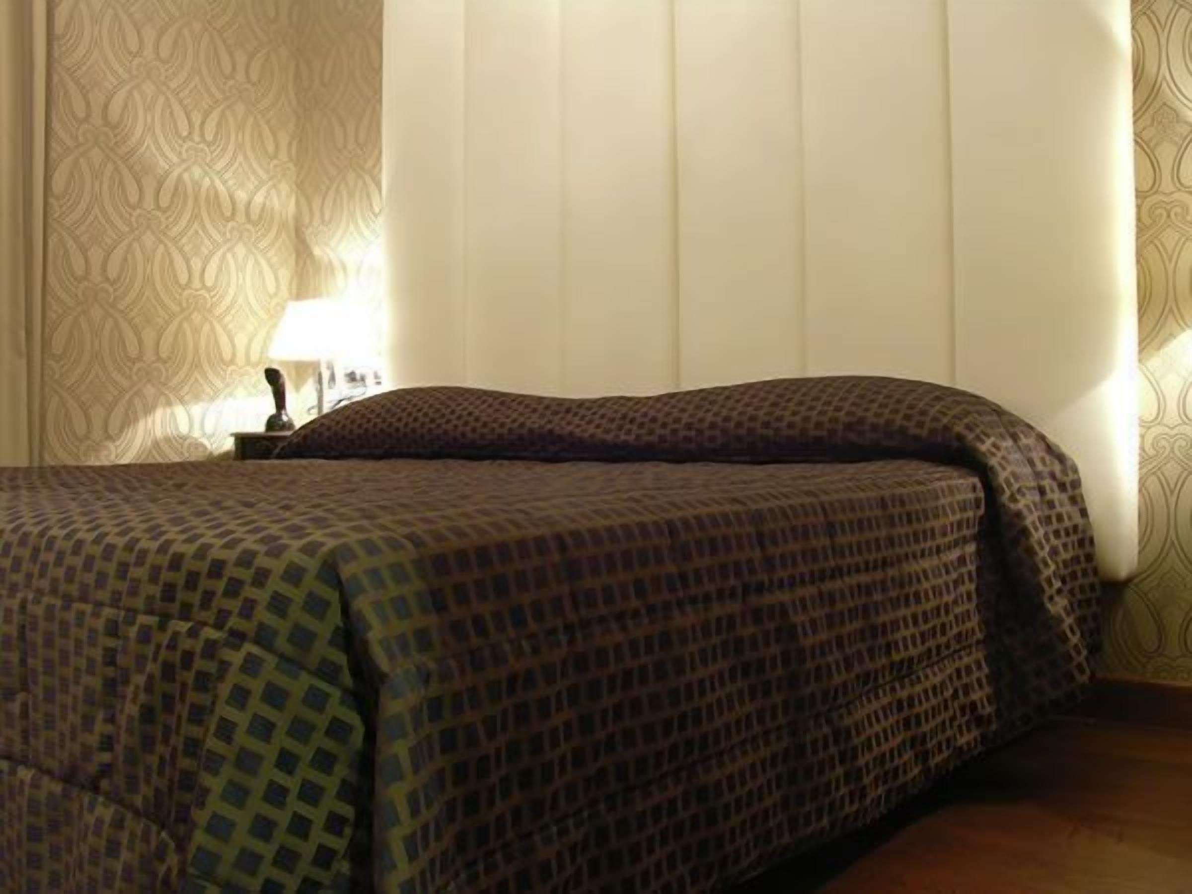A hotel room with a bed, a nightstand, and a lamp.