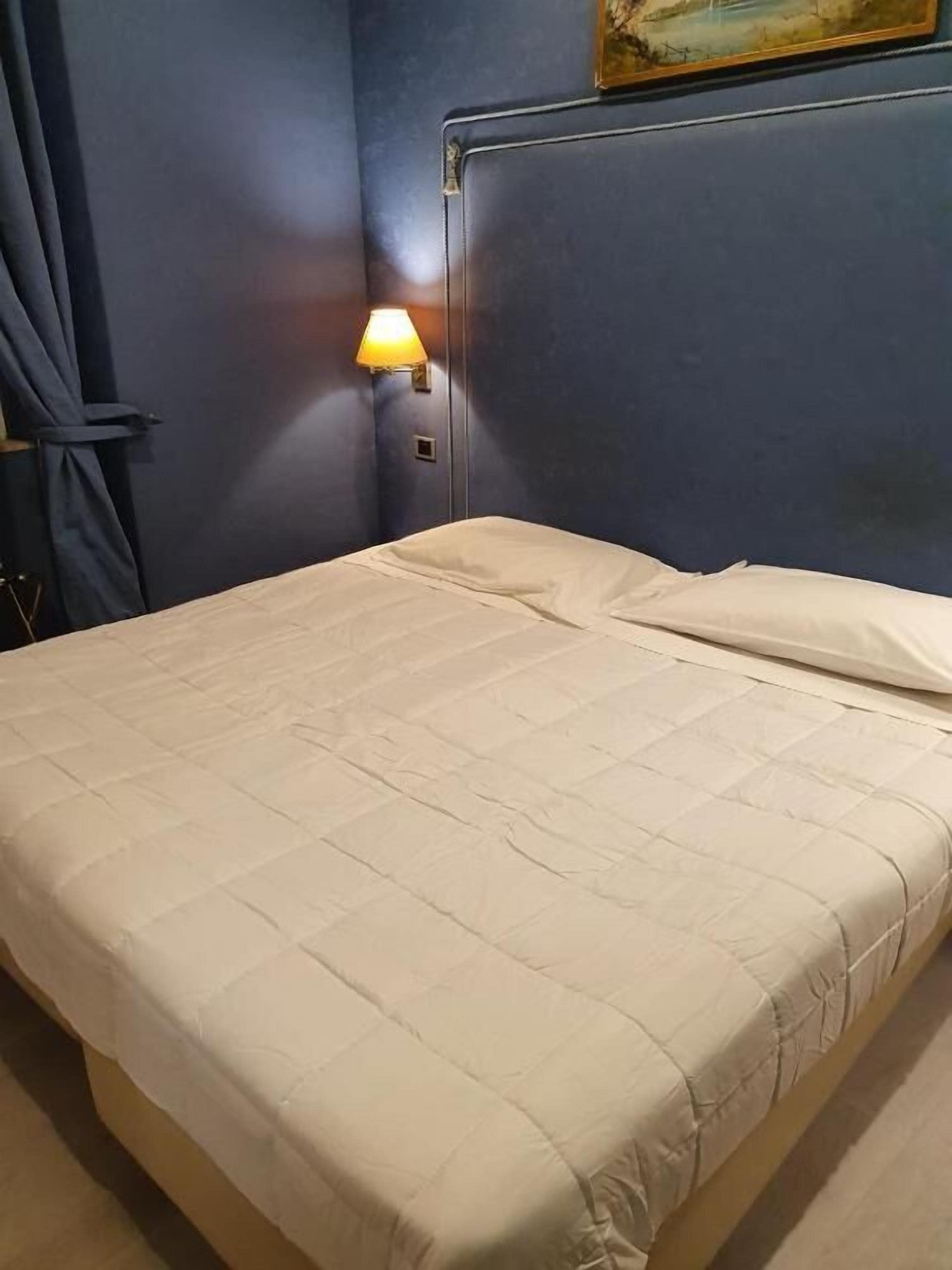 Een net opgemaakt bed met een gewatteerde spreidek, in een kamer met een donkerblauwe wand en een schilderij erboven.