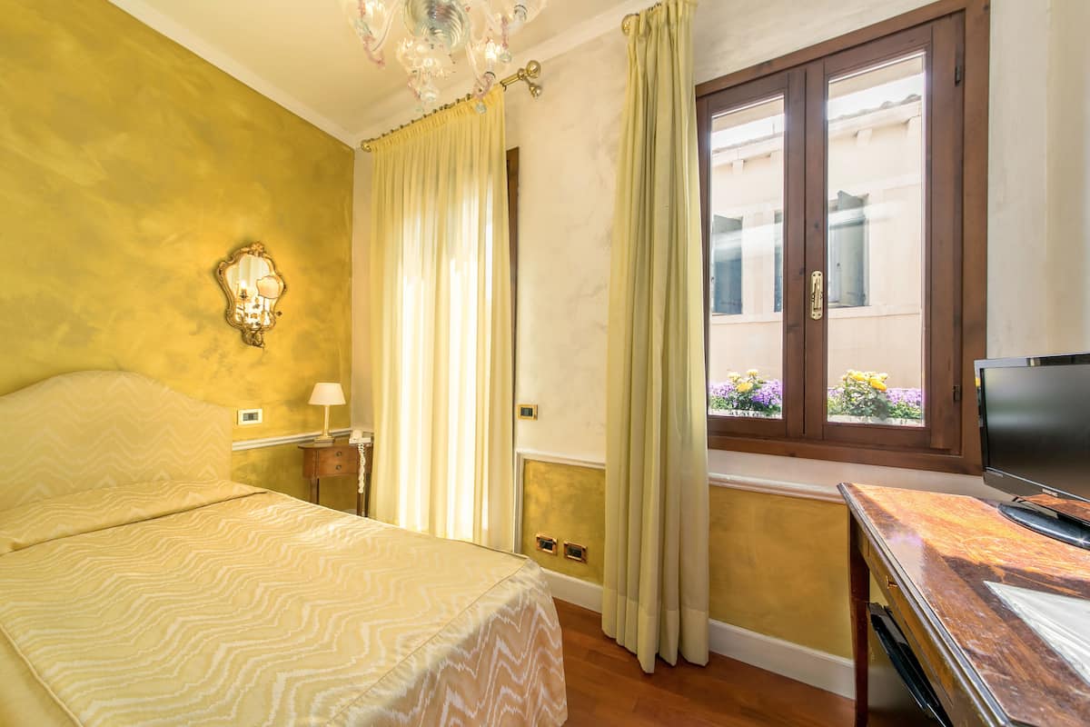 A hotel room with a bed, a television, a window with curtains, and a wall-mounted light fixture.