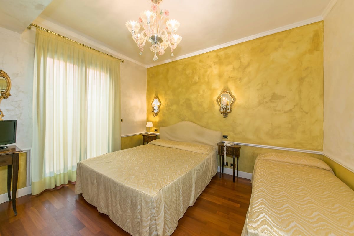 A hotel room with two beds, a chandelier, and a television on a desk.