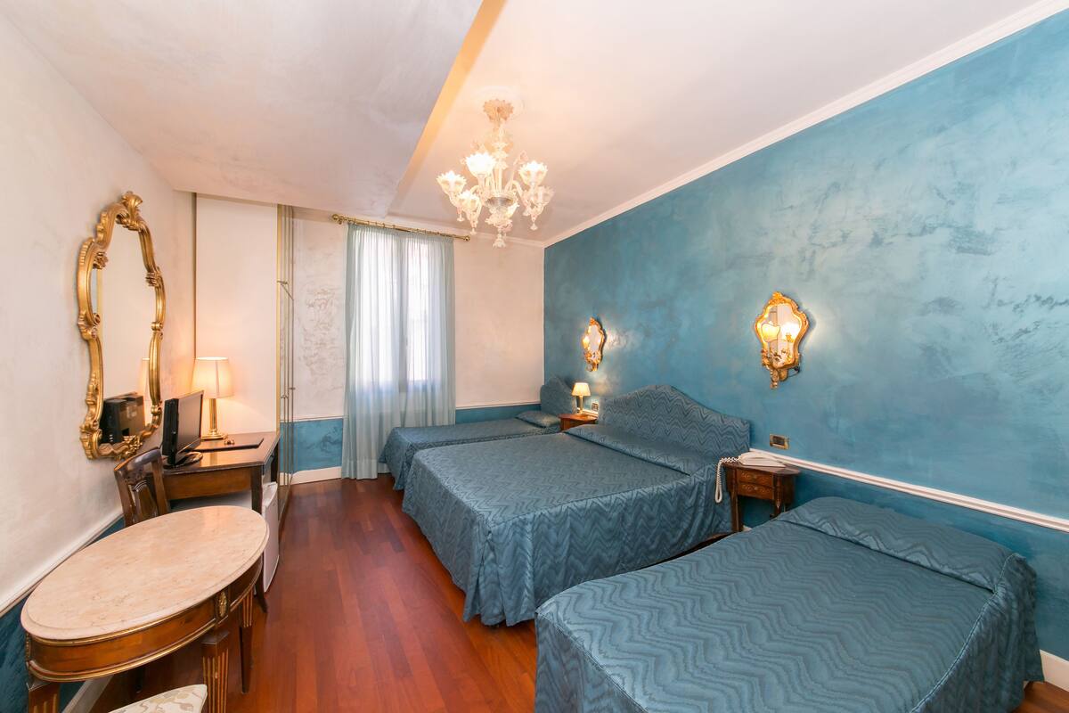 A hotel room with two beds, a vanity with a mirror, a desk, and a chandelier.