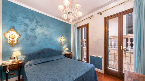 A bedroom with a large bed, two bedside tables with lamps, a chandelier, and a balcony with a view. - Pantalon Hotel (Venice)
