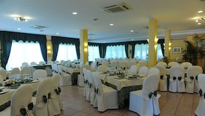 A banquet hall with round tables, white chairs with green sashes, and a tiled floor. - Hotel Orizzonte (Acireale)