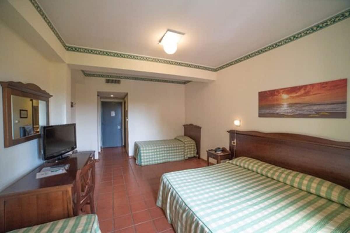 Une chambre d’hôtel avec deux lits simples, un téléviseur posé sur un bureau en bois, un tableau accroché au mur et un sol carrelé.