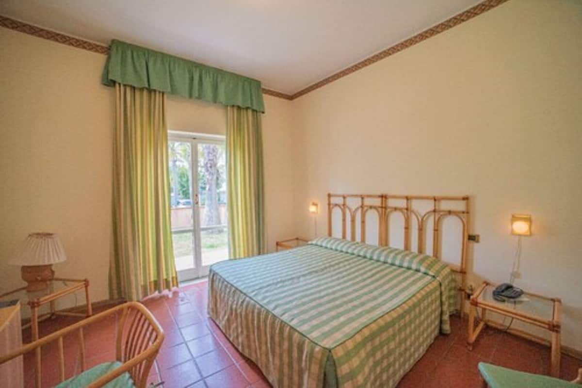 Une chambre à coucher avec un lit, une chaise, une table de chevet et une fenêtre avec des rideaux.