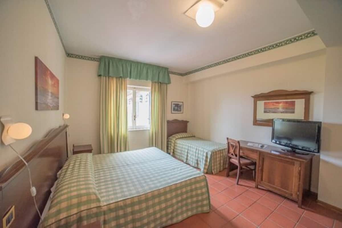 Une chambre d’hôtel avec deux lits, un bureau, une télévision et une fenêtre avec des rideaux.