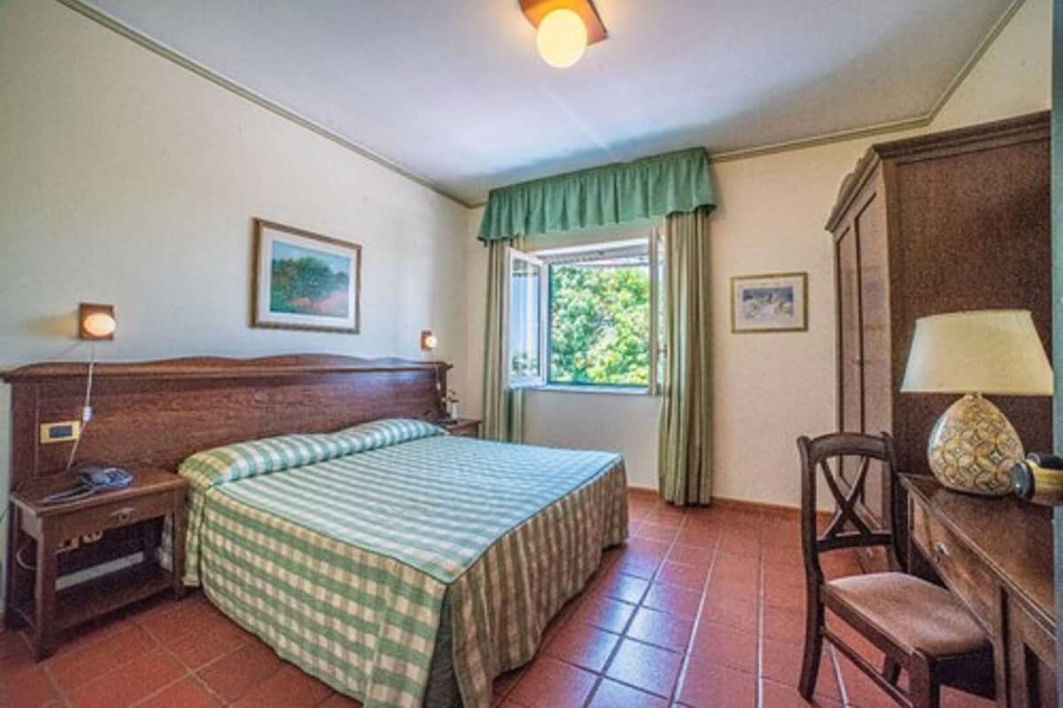 Une chambre à coucher comprenant un lit, une table de chevet, un bureau avec une lampe, une chaise et une fenêtre avec des rideaux.