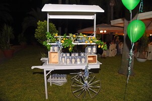 Un carrito exterior blanco con frascos de comida y flores, sobre césped.