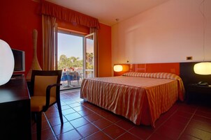 Habitación de hotel con cama, escritorio, silla, mesa y balcón con vistas.