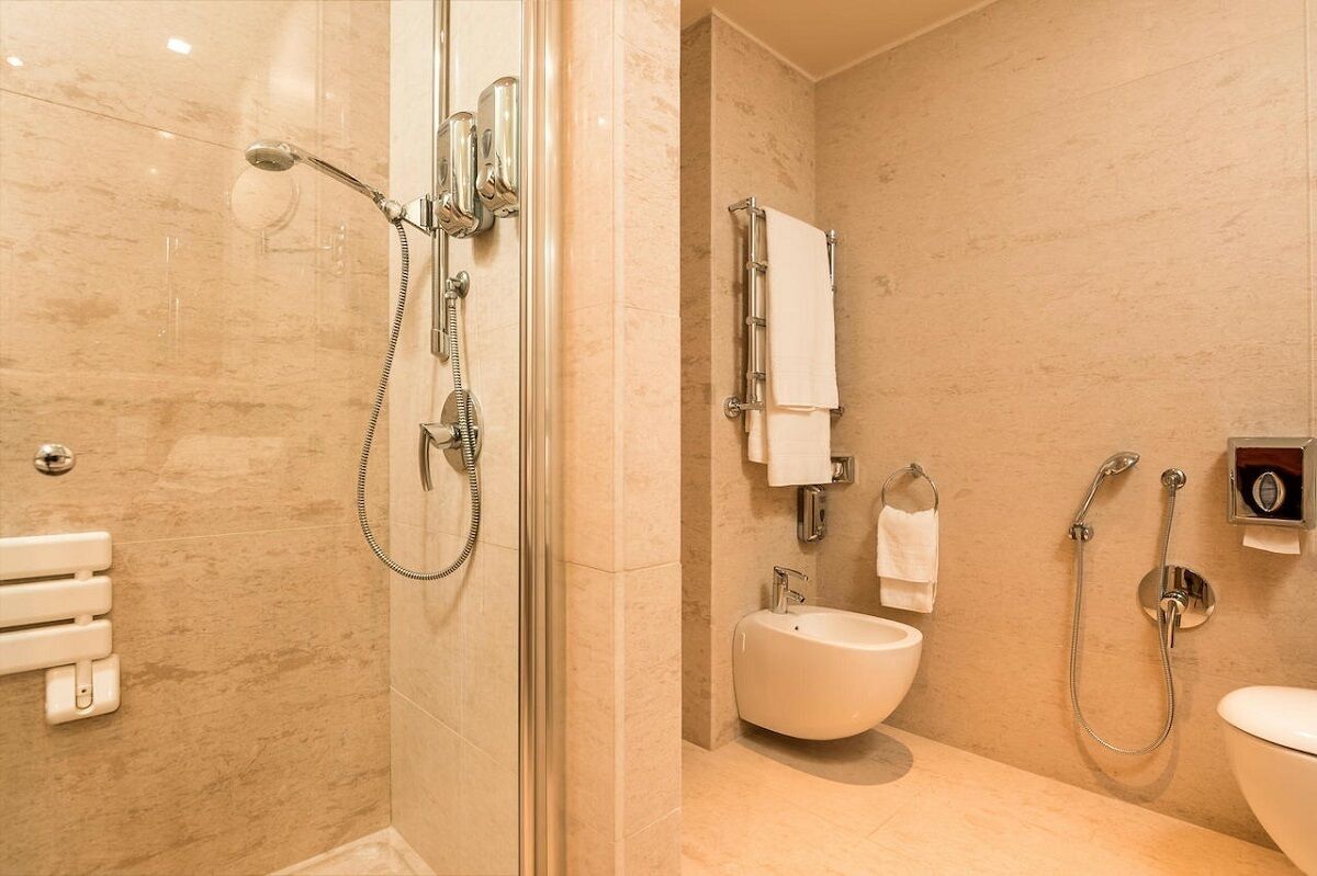 A modern bathroom with a glass-enclosed shower, a bidet, and a toilet.