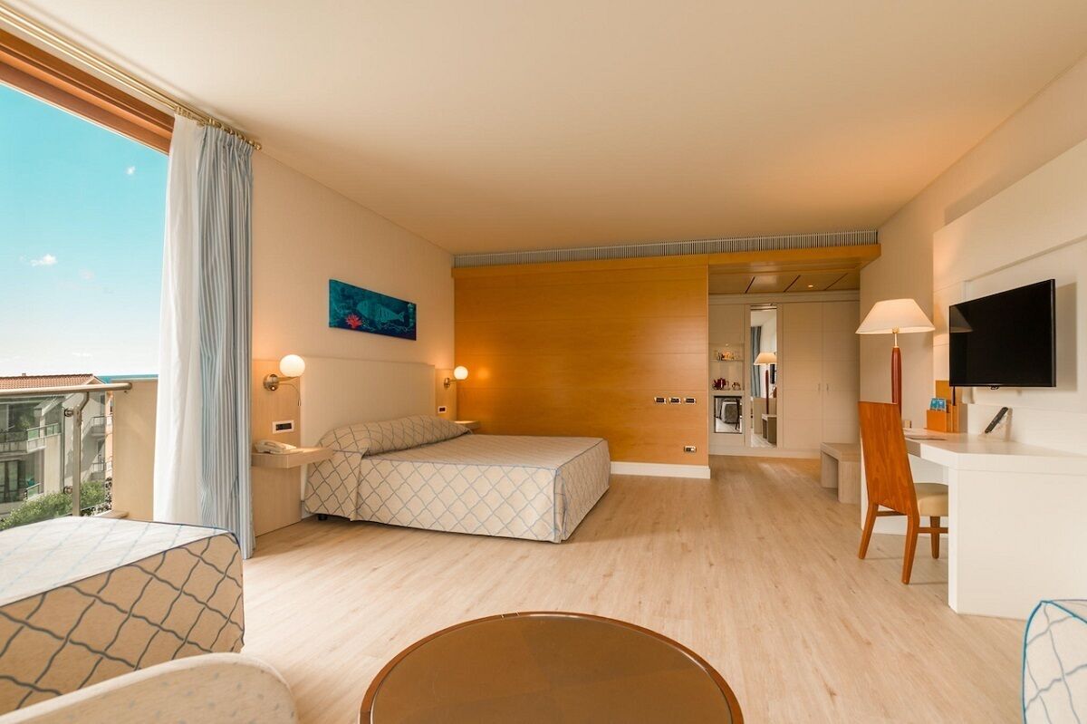Een hotelkamer met een bed, bureau, stoel, televisie en een badkamer zichtbaar door een geopende deur.
