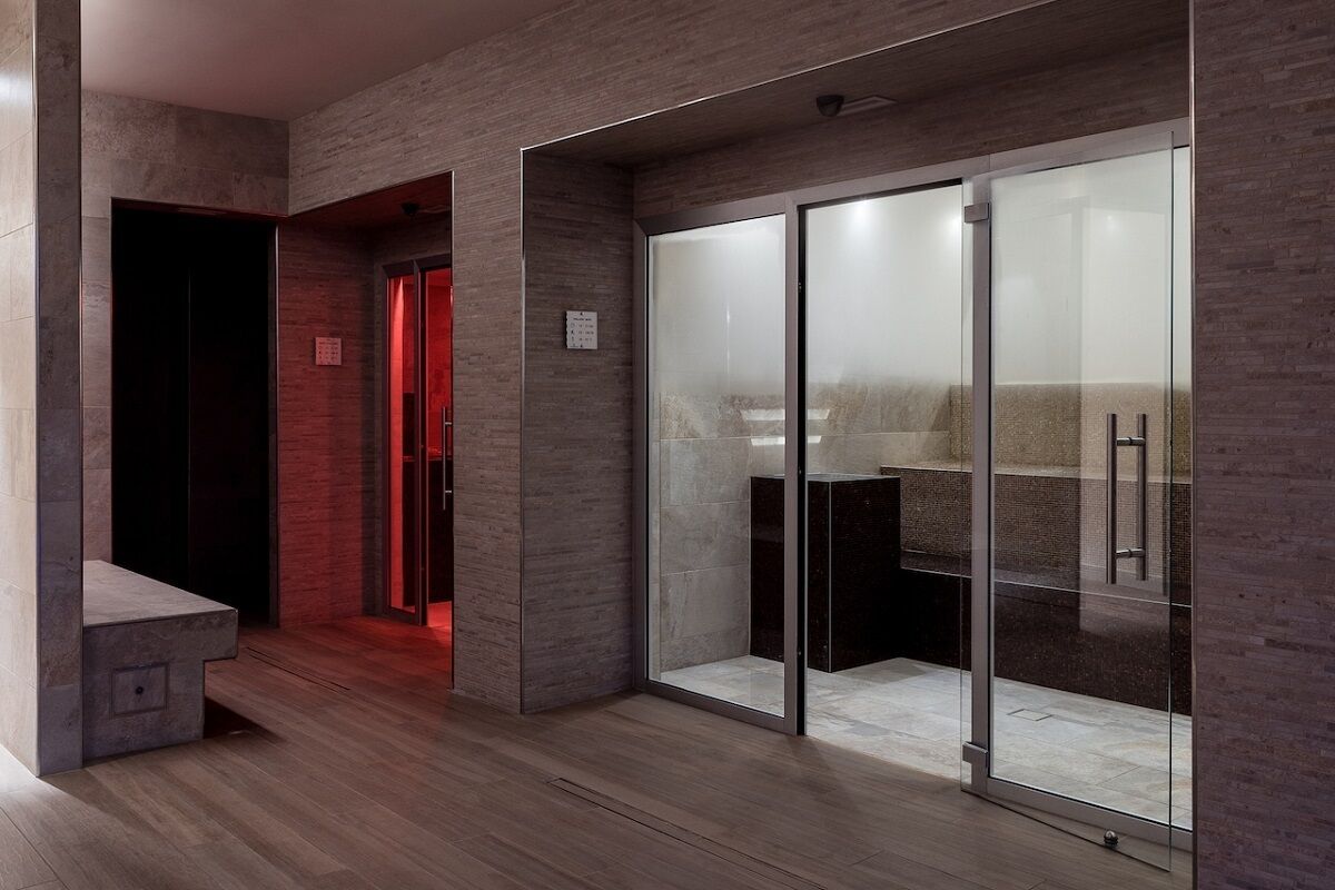 A modern interior with a glass door leading to a bathroom, a wooden floor, and a red-lit hallway.