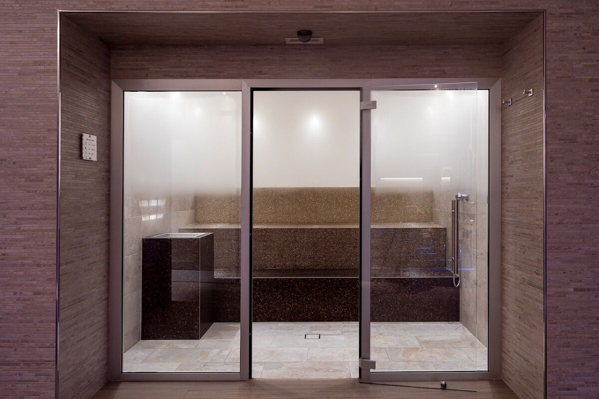 A modern shower enclosure with glass doors, a bench, and a control panel.