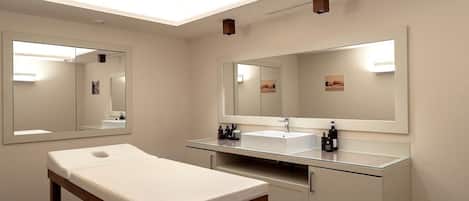 A modern bathroom with a large mirror, a white sink, and a wooden bench.