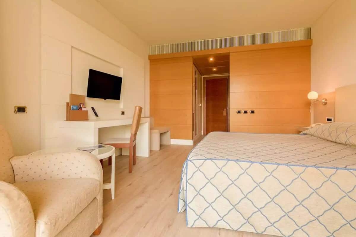 A hotel room with a bed, a desk, a chair, a TV, and a door leading to another room.